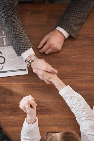 High angle view of business couple shaking hands to each other at the wooden table during a meeting