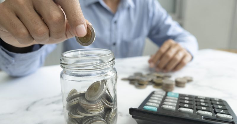 Businessman saving money concept. Hand holding coins putting in jug glass